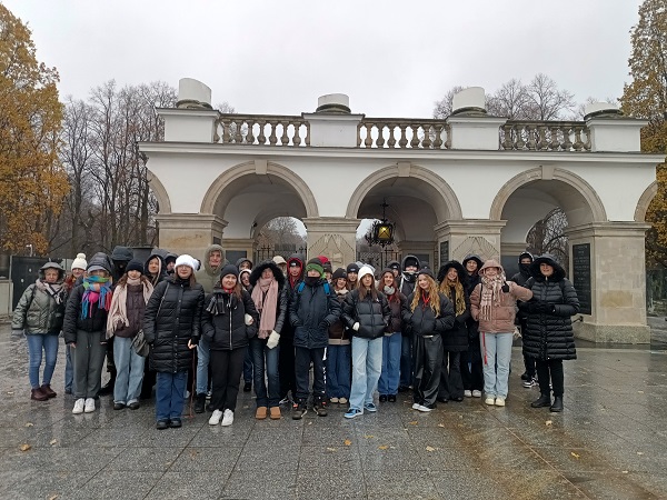 Zdjęcie przedstawia grupę uczniów i nauczycieli na tle bramy.