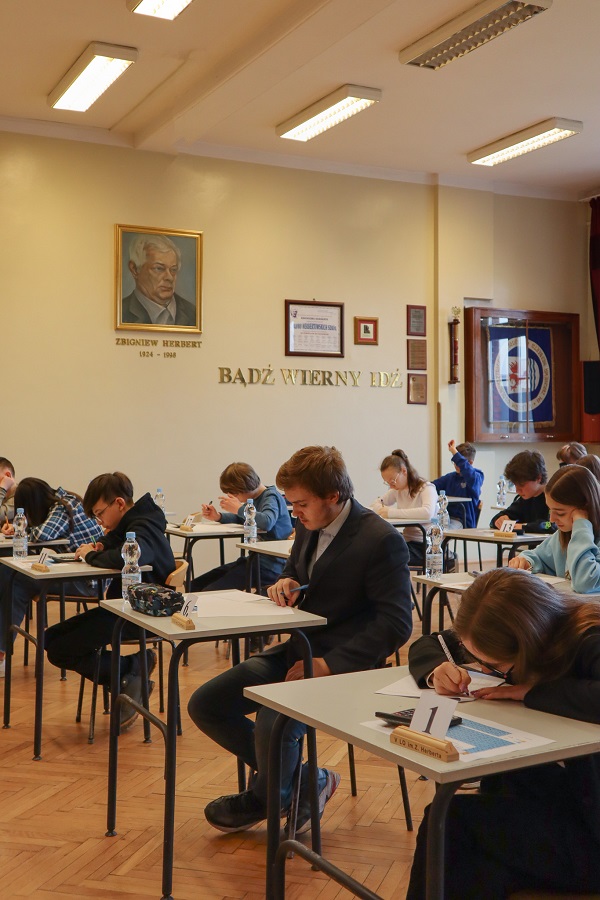 Zdjęcie przestawia uczniów siedzących w ławkach i piszących test konkursowy.